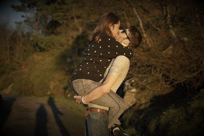 Side view of young couple kissing on road against trees