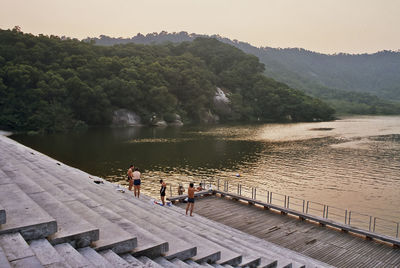 People standing on steps by lake against clear sky