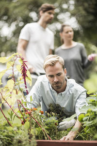 Man gardening while friends standing in background at garden