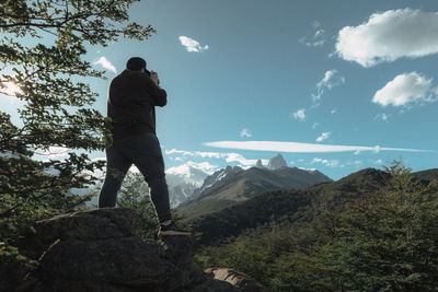 Rear view of man standing on mountain against sky