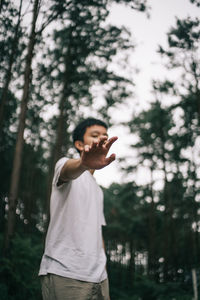 Low angle view of boy showing stop gesture against trees