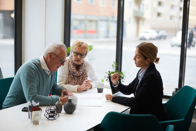 Senior man with woman signing property document while sitting with agent in real estate office
