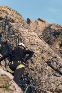 Concept: adventure. climber woman with helmet and harness. backwards. resting before continuing climbing. via ferrata in the mountains.