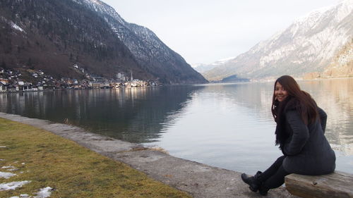 Portrait of woman sitting by lake against mountains