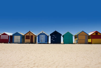 Beach huts against buildings against clear blue sky