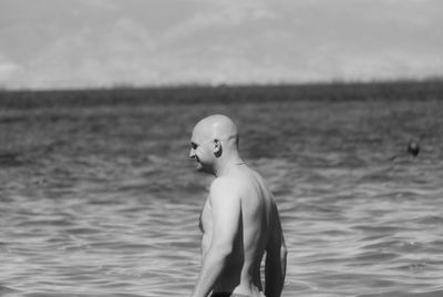 Side view of shirtless man standing in sea against sky during sunny day