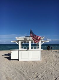 American flag waving on lifeguard hut at beach against blue sky