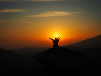 Silhouette woman sitting on mountain against sky during sunset