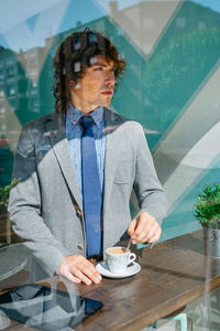 Businessman having coffee at cafe seen through glass