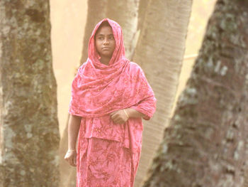 Portrait of young woman standing against trees 