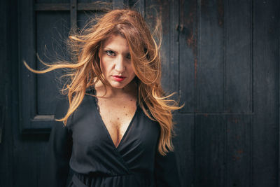 Portrait of mature woman with tousled hair standing against wall