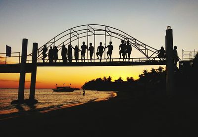 Silhouette people on bridge against clear sky during sunset