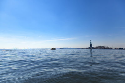 Scenic view of the hudson river against blue sky with the statue of liberty on the horizon.