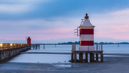 Lighthouse by sea against sky during sunset