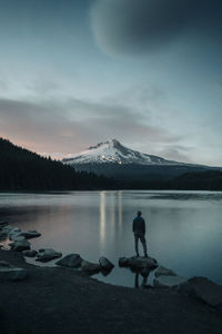 A young woman stands on the edge of trillium lake in oregon.