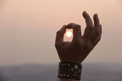 Close-up of hand holding sun against sky during sunset