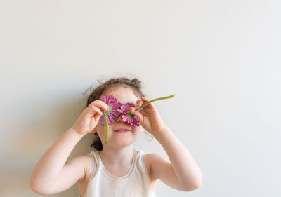 Playful girl holding purple flowers against wall