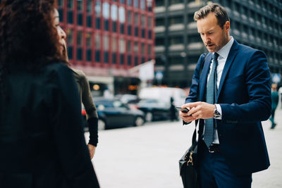 Man using phone while standing on street in city