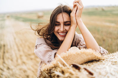 Close-up of smiling young woman with eyes closed by hay bale