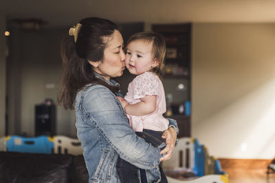Portrait of mother hodling daughter and kissing her cheek