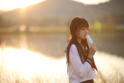 Young woman standing against lake during sunset