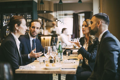 Male and female professionals talking while sitting for business lunch in restaurant