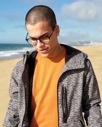 Man wearing eyeglasses standing at beach against sky