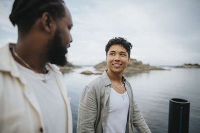 Smiling man looking at male friend while walking near lake
