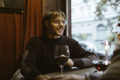 Gay man wearing eyeglasses and talking with boyfriend while sitting at restaurant