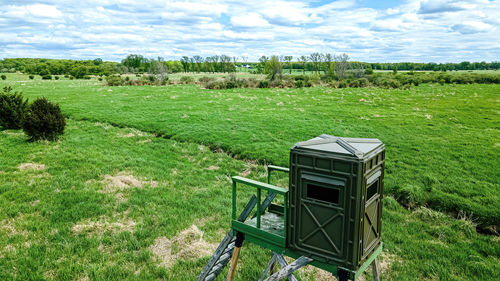Spring with a cloudy blue sky above a  green field. a hunting blind stands over looking all of it