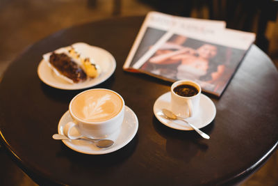 Close up a mug of fragrant cappuccino and a sweet dessert and a magazine on the table