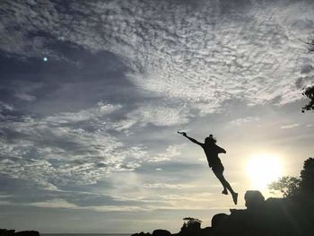 Silhouette man jumping on rock against sky during sunset