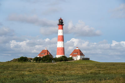 Lighthouse on field by building against sky