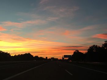 Road by silhouette trees against sky during sunset