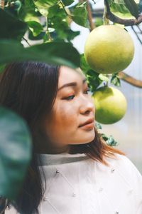Close-up of young woman standing by fruit on tree