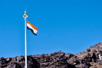 Low angle view of indian flag on rock against clear blue sky