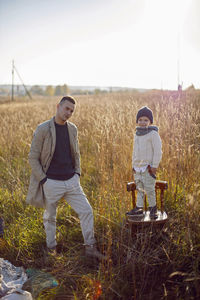 Father and son are standing on a field with dry grass outside the city in autumn