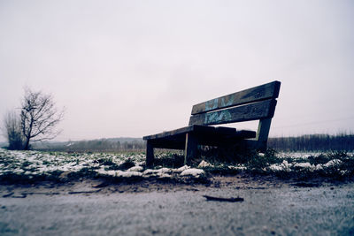 Empty bench on field against sky