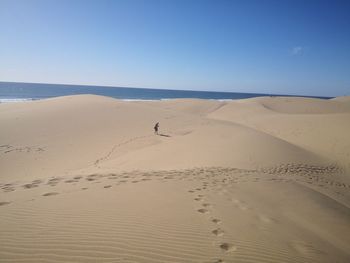 Footprints on sand in desert against clear sky