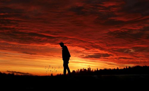 Silhouette man standing on field against sky during sunset