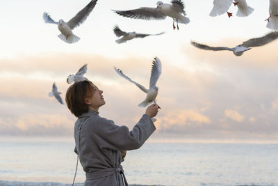 Young woman feeding seagulls at beach