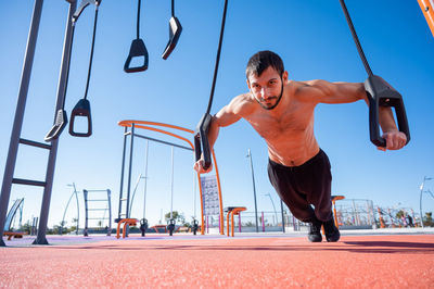 Shirtless man doing exercise with rubber bands outdoors. 