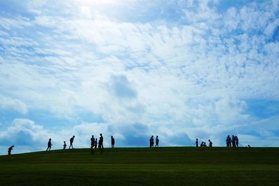 People on grassy field against cloudy sky
