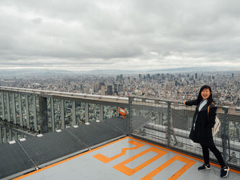 Portrait of woman standing on building terrace against cloudy sky