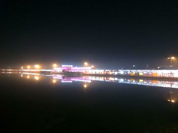 Illuminated city by river against clear sky at night