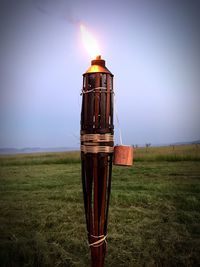 Tiki torch burning on grassy field against sky at dusk