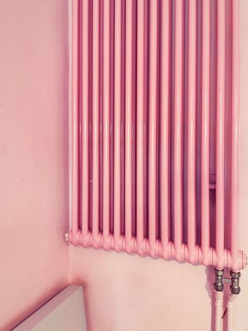 Close-up of pink radiator pipes on wall in building