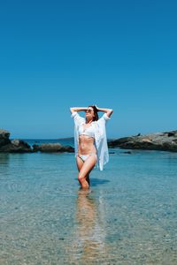 Full length of young woman in sea against clear blue sky