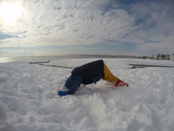 Side view of boy playing on snow covered beach against cloudy sky