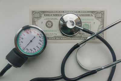 High angle view of stethoscope with pressure gauge and currency on table